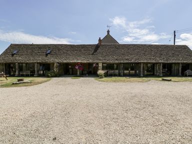 A stone building with a long sloped roof and gravel driveway at Tinkley Cottage in Nympsfield near Nailsworth