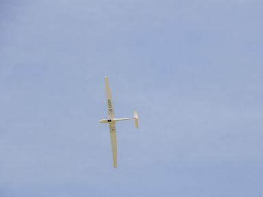 A white glider aircraft flying in a clear blue sky