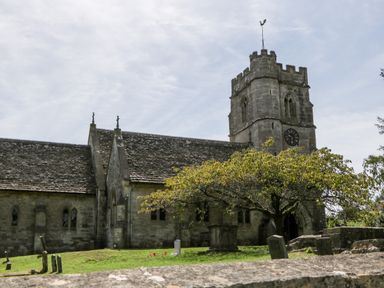 An old stone church with a clock tower and gravestones in the yard at Tinkley Cottage in Nympsfield near Nailsworth