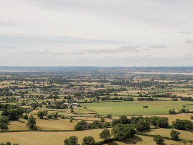 A rural landscape with fields divided by hedges and trees and a small village in the distance at Tinkley Cottage in Nympsfield near Nailsworth