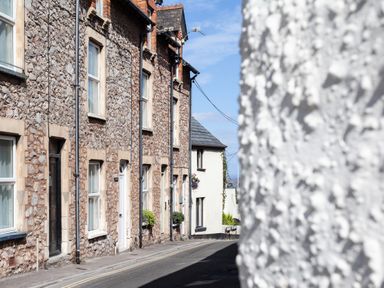 Stone and brick houses along a quiet street with paved sidewalk and white building in background at Sea Spray in Watchet