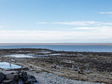 A rocky beach with tidal pools and people walking near the sea at Sea Spray in Watchet