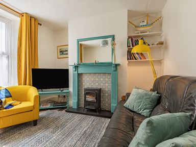 A living room with a teal fireplace black stove yellow armchair and black sofa with green cushions at Sea Spray in Watchet