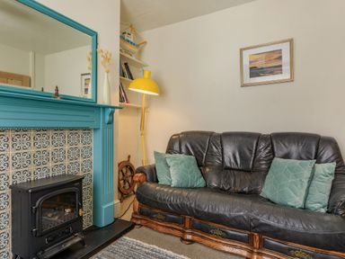 A living room with a black leather sofa green cushions a yellow floor lamp blue mantelpiece with a mirror and a wall painting at Sea Spray in Watchet
