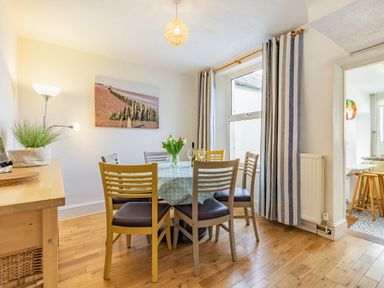 A dining room with a wooden table and six chairs with a vase of flowers and wine glasses at Sea Spray in Watchet