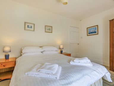 A bedroom with a double bed white linens two bedside tables with lamps three paintings on walls and folded towels on bed at Sea Spray in Watchet