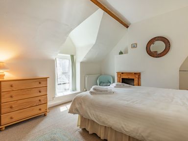 A bedroom with a wooden chest of drawers a bed with folded towels a small fireplace and a window at Sea Spray in Watchet