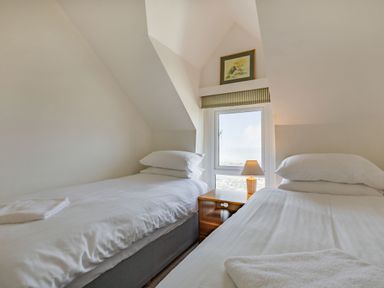 A bedroom with two single beds a nightstand with a lamp and a window with a striped valance at Sea Spray in Watchet