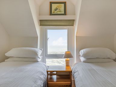 A bedroom with two single beds separated by a wooden nightstand with a lamp and a window in the middle at Sea Spray in Watchet