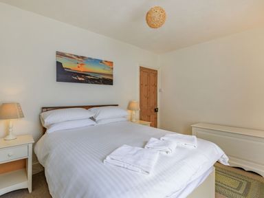 A bedroom with a large bed and white linens next to two nightstands with lamps at Sea Spray Watchet