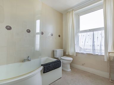 A bathroom with a bathtub toilet window with curtains and a towel on the bathtub at Sea Spray in Watchet