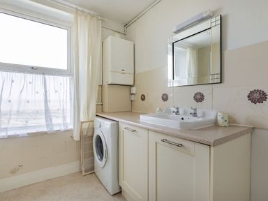 A utility room with a washing machine under a counter and a sink with a mirror above Sea Spray Watchet