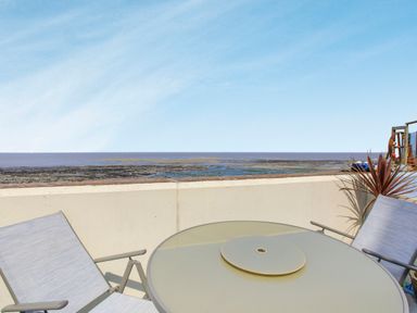 An outdoor patio with two chairs and a round glass table overlooking the ocean at Sea Spray in Watchet
