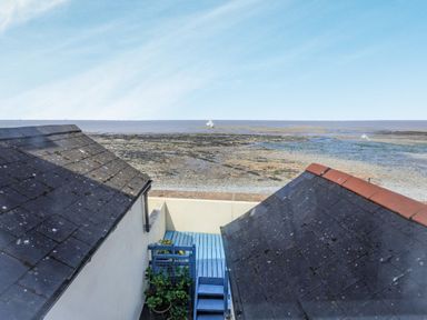 A blue wooden deck between two rooftops overlooking a rocky shore and the sea at Sea Spray in Watchet