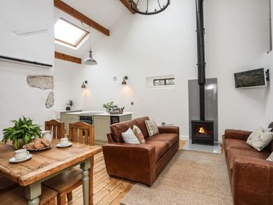 A living room with two brown leather sofas a fireplace a wooden dining table with chairs and a small kitchen area at Yr Hen Oriel in Llanrug
