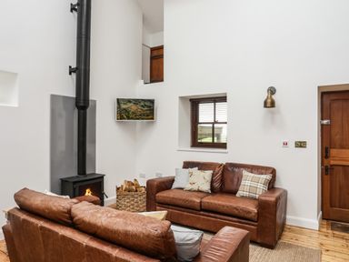 A living room with two brown leather sofas a wood-burning stove and a wooden door at Yr Hen Oriel in Llanrug