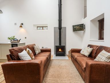 A living room with two brown leather sofas facing a wood burning stove and a television mounted on the wall at Yr Hen Oriel in Llanrug
