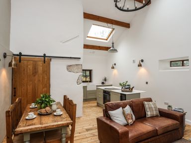 A kitchen and dining area with wooden table, leather sofa, skylight, and wooden beams at Yr Hen Oriel in Llanrug
