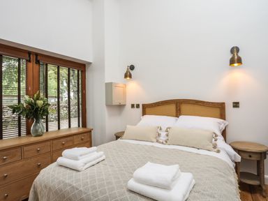 A bedroom with a double bed two pillows folded towels wooden dresser with flowers and bedside tables at Yr Hen Oriel in Llanrug