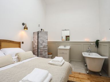 A bedroom with a bed pillows towels a bathtub a sink a mirror and a partition at Yr Hen Oriel in Llanrug