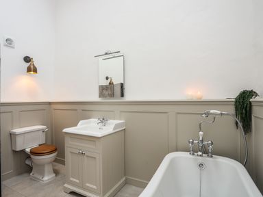 A bathroom with a toilet a sink a bathtub with a handheld shower and candles on the ledge at Yr Hen Oriel in Llanrug