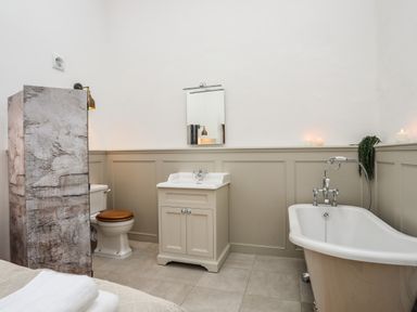 A bathroom with a freestanding bathtub a sink with cabinet a toilet and a partition wall at Yr Hen Oriel in Llanrug