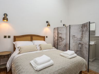 A bedroom with a bed towels bedside table wall lamps and room divider at Yr Hen Oriel in Llanrug