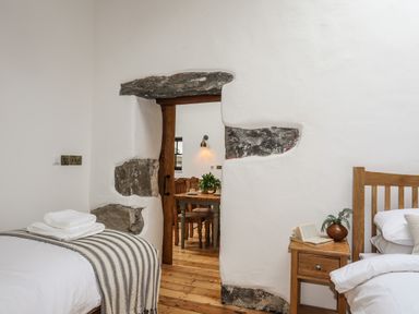 A bedroom with two beds and a wooden door leading to a dining area at Yr Hen Oriel in Llanrug