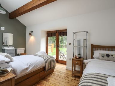 A bedroom with two single beds a wooden floor and glass doors leading outside at Yr Hen Oriel in Llanrug
