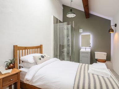 A bedroom with a wooden bed next to a bedside table and an open book a shower stall a sink with a mirror and a toilet at Yr Hen Oriel in Llanrug