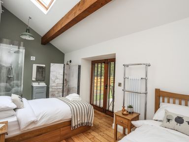 A bedroom with two single beds wooden flooring and doors at Yr Hen Oriel in Llanrug