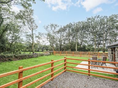 A fenced grassy yard with outdoor table and chairs next to a stone building at Yr Hen Oriel in Llanrug