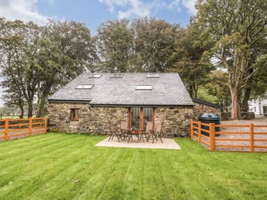 A stone house with a slate roof and skylights a patio table with chairs on a lawn surrounded by trees at Yr Hen Oriel in Llanrug