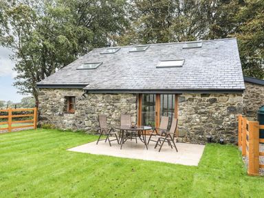 A stone house with skylights and wooden framed glass doors next to a patio with a table and four chairs at Yr Hen Oriel in Llanrug
