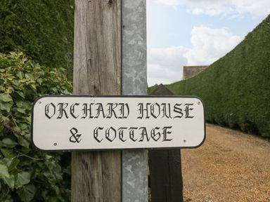 A wooden post with a sign reading Orchard House and Cottage on a gravel path with hedges on either side at Orchard House Cottage in Malmesbury