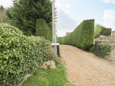 A gravel driveway bordered by tall trimmed hedges and a wooden post with a sign at Orchard House Cottage in Malmesbury