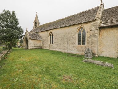 An exterior view of a stone church building with pointed arched windows and green grass surrounding it at Orchard House Cottage in Malmesbury