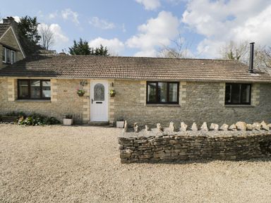 A stone cottage with a white door and three windows a stone wall and gravel driveway outside at Orchard House Cottage in Malmesbury