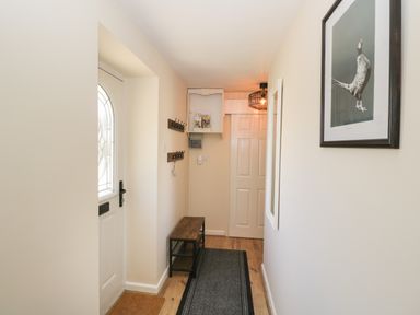 A hallway with a white door a wooden bench coat hooks a hanging light and a bird picture on the wall at Orchard House Cottage in Malmesbury