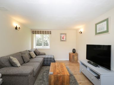 A living room with a gray sofa wooden coffee table television and framed pictures at Orchard House Cottage in Malmesbury