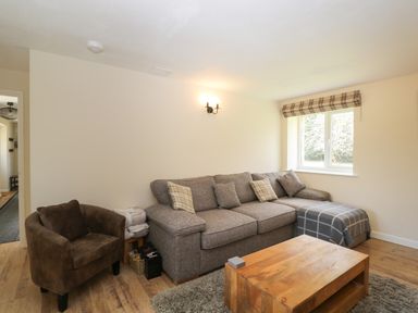 A living room with a gray sectional sofa and a brown armchair with a wooden coffee table at Orchard House Cottage in Malmesbury