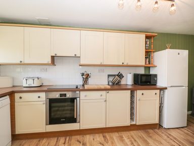A kitchen with cream cabinets wooden countertop built in oven toaster microwave and refrigerator at Orchard House Cottage in Malmesbury