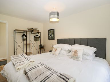 A bedroom with a double bed pillows and blankets a stand with hangers and a wall mirror at Orchard House Cottage in Malmesbury