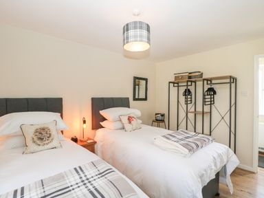 A bedroom with two single beds pillows a nightstand with a lamp open wardrobe and a small round stool at Orchard House Cottage in Malmesbury