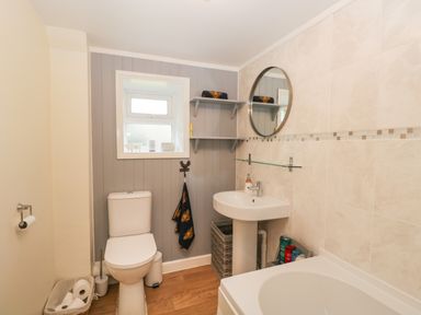A bathroom with a toilet sink round mirror shelves and bathtub at Orchard House Cottage in Malmesbury
