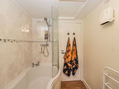 A bathroom with a bathtub shower combination and towels hanging on a door at Orchard House Cottage in Malmesbury