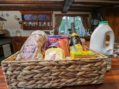 A kitchen counter with a basket containing bread butter cheese a bottle of prosecco and a can next to a milk container at Orchard House Cottage in Malmesbury