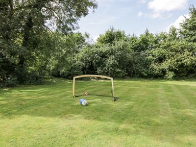A small soccer goal with two soccer balls on a grassy field surrounded by trees at Orchard House Cottage in Malmesbury