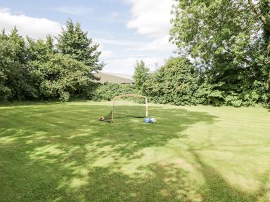 A grassy backyard with a small soccer goal and three balls surrounded by trees at Orchard House Cottage in Malmesbury