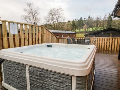 An outdoor hot tub on a wooden deck with table and chairs surrounded by wooden fencing and trees at Wansfell View in Limefitt Park near Troutbeck